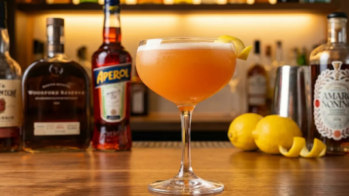 Paper Plane cocktail served in a chilled coupe glass with a vibrant orange color and smooth citrus foam