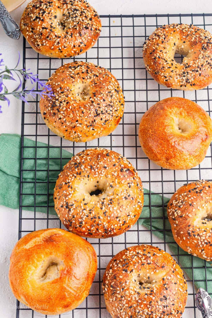 Sourdough Bagel Recipe 12 Freshly baked sourdough bagels topped with sesame and everything seasoning, cooling on a wire rack with a golden crust. - Sourdough Bagel Recipe
